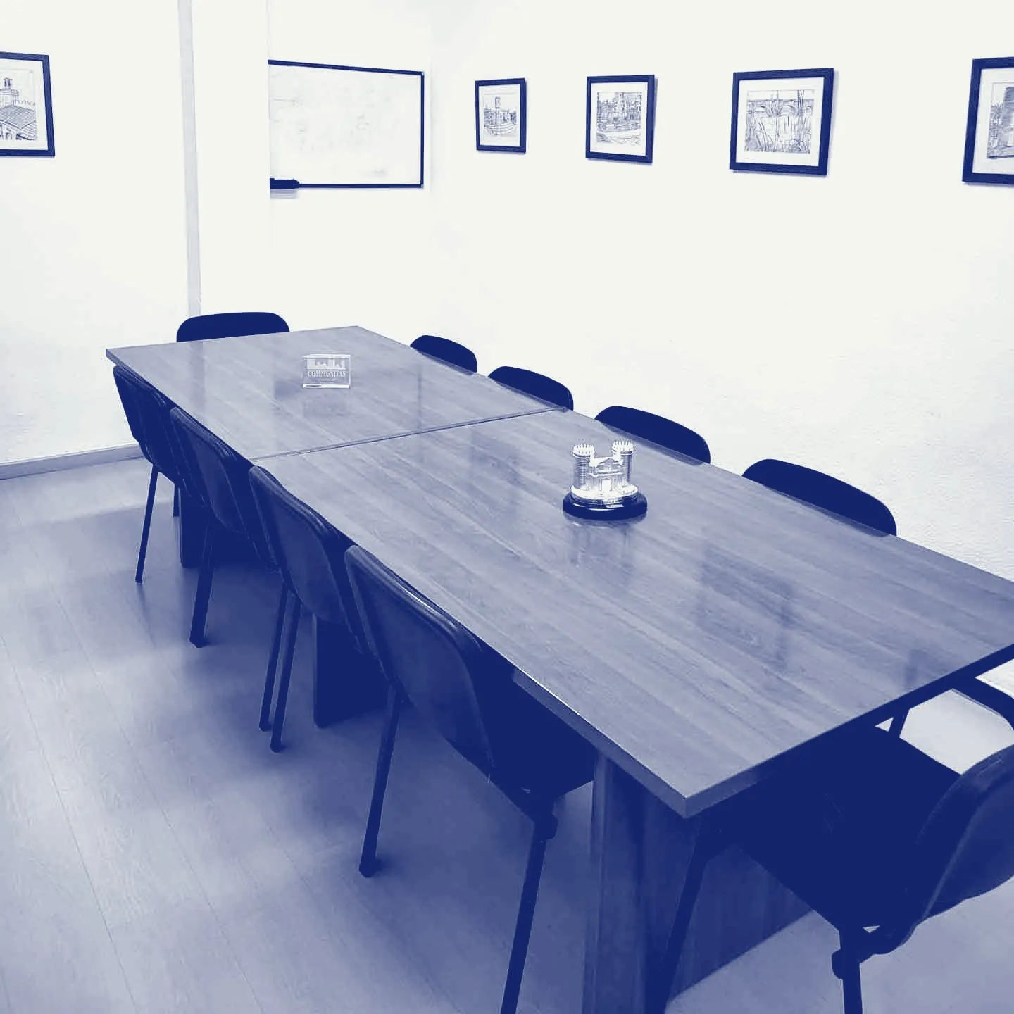 Sala de reuniones del despacho: mesa de madera con sillas y dibujos enmarcados de rincones de Badajoz en la pared.